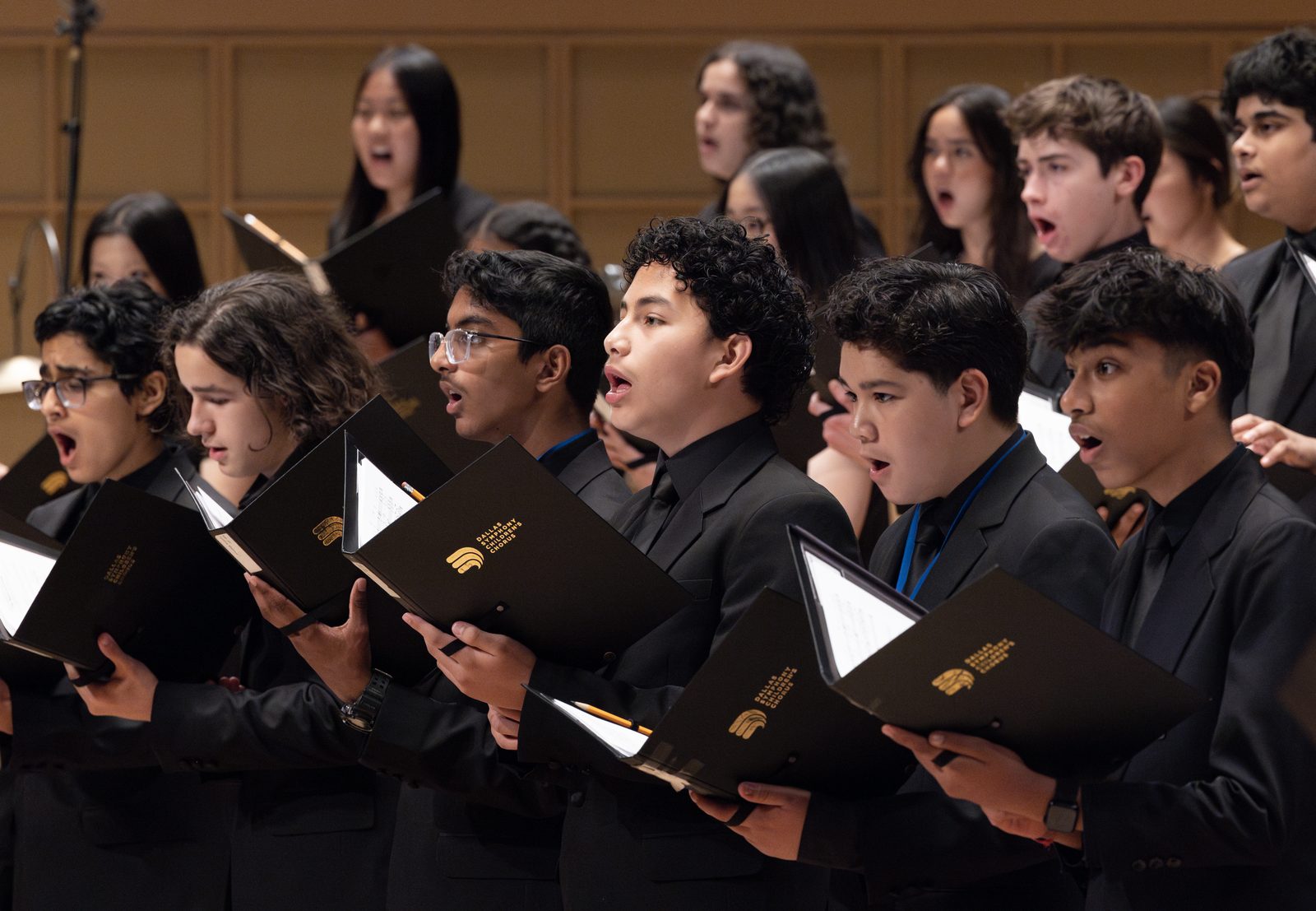 Mixed Ensemble choristers in black suits singing from folders marked Dallas Symphony Children&rsquo;s Chorus