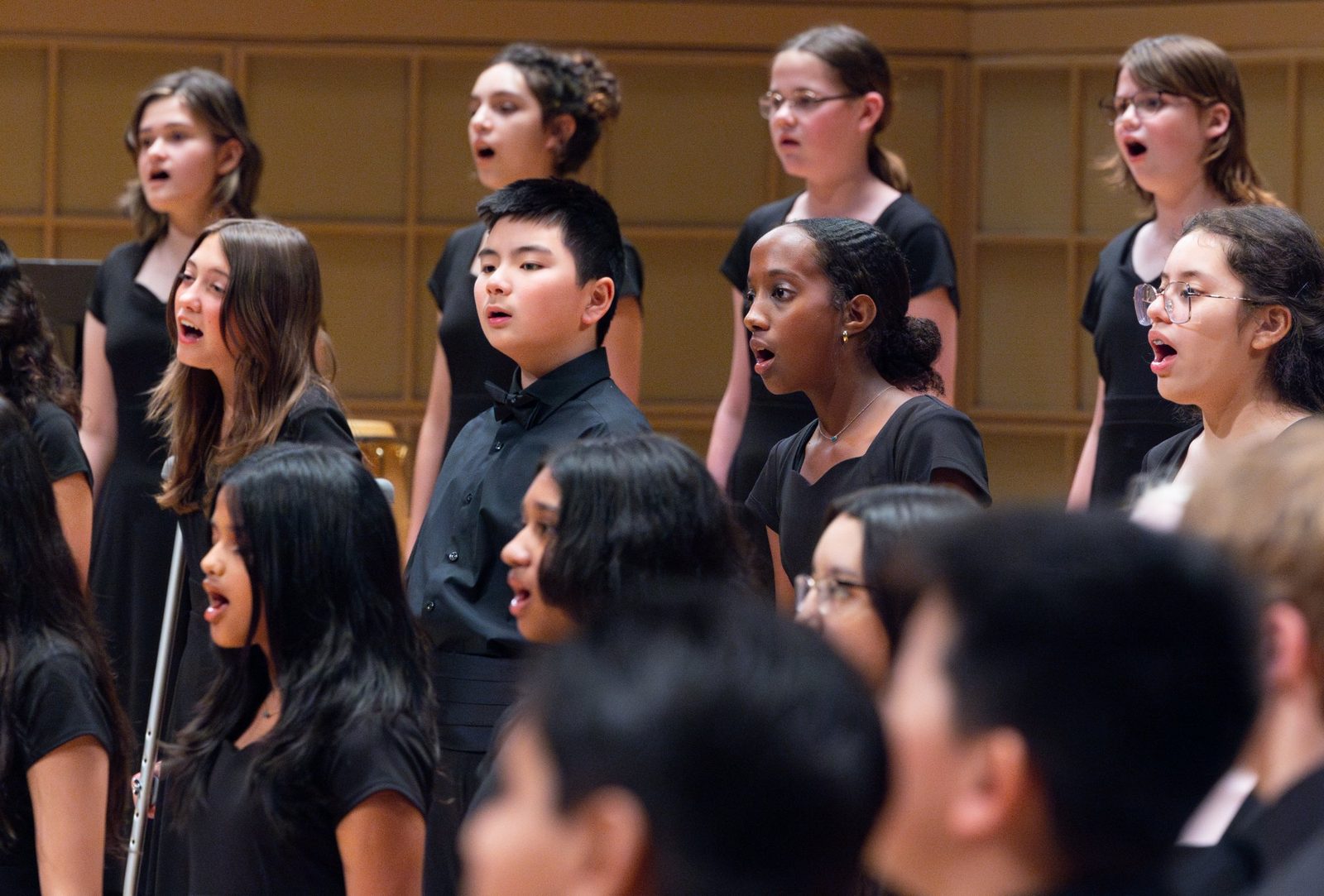 Symphonic Voices choristers singing in two rows on stage, with a boy in a bow tie standing among the girls