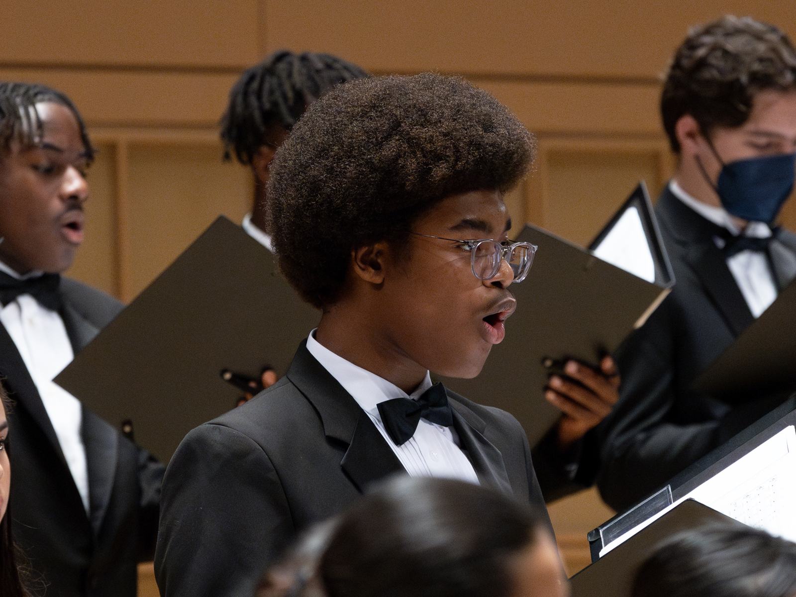 Choristers in formal concert attire singing from their folders on stage