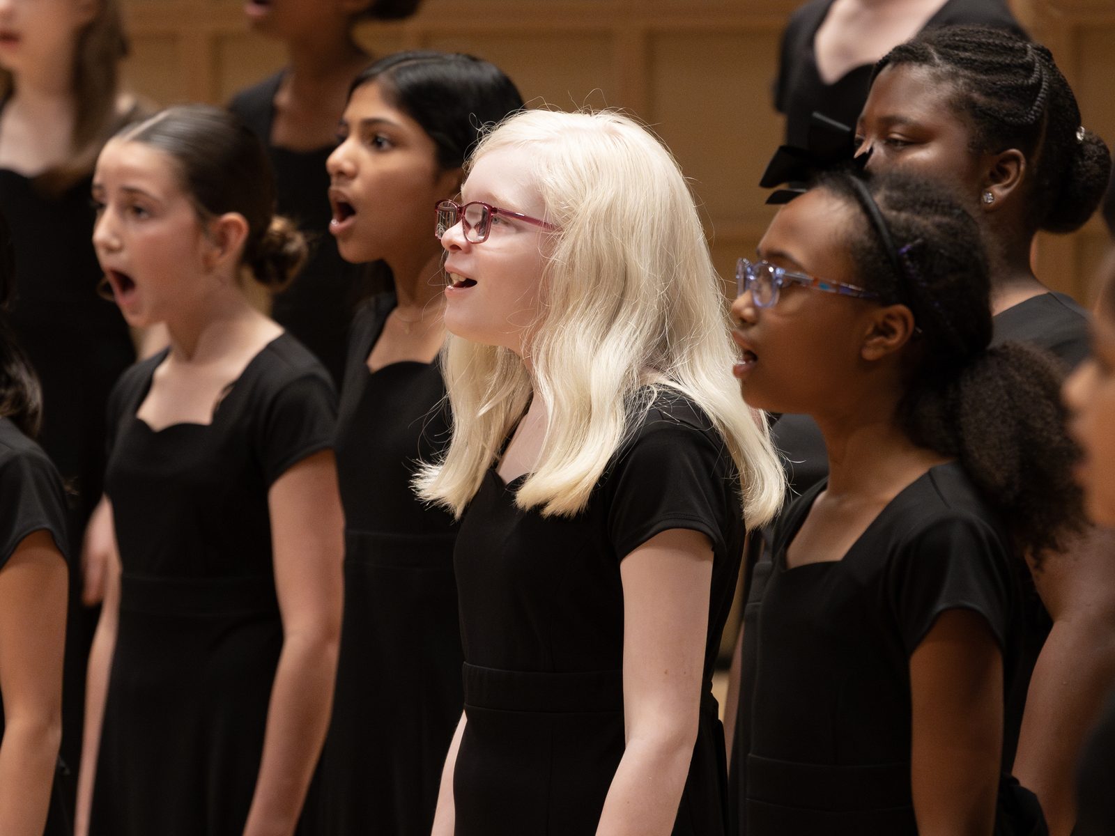 Choristers in black concert attire singing together on stage, faces lifted in song